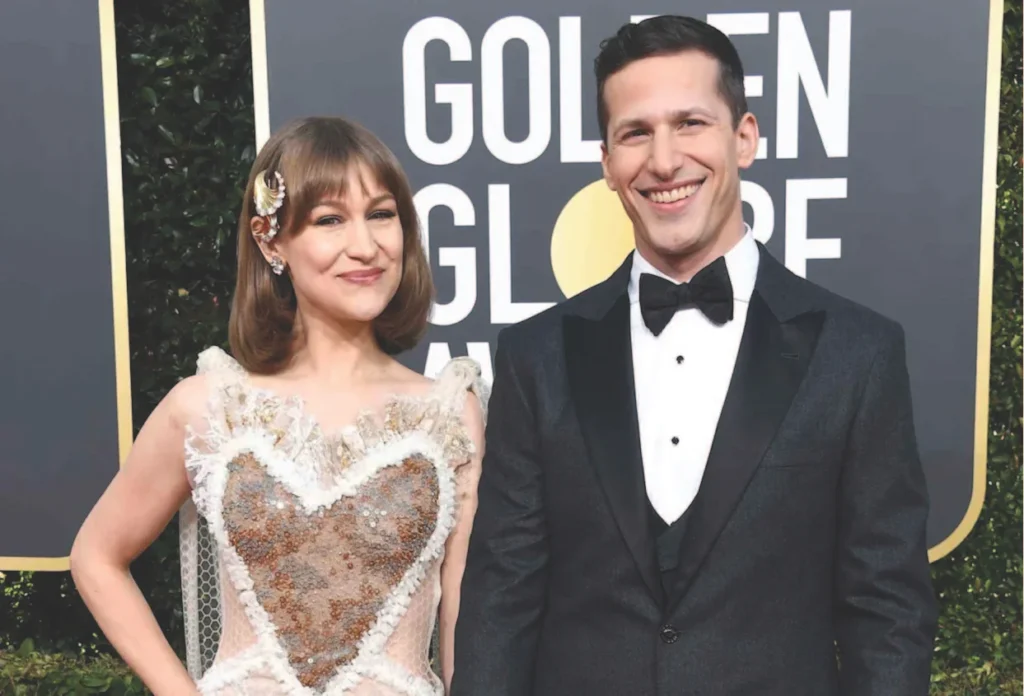 A couple poses together at the Golden Globe Awards. johanna samberg wears a sparkling heart-shaped dress, and the man is in a classic tuxedo.